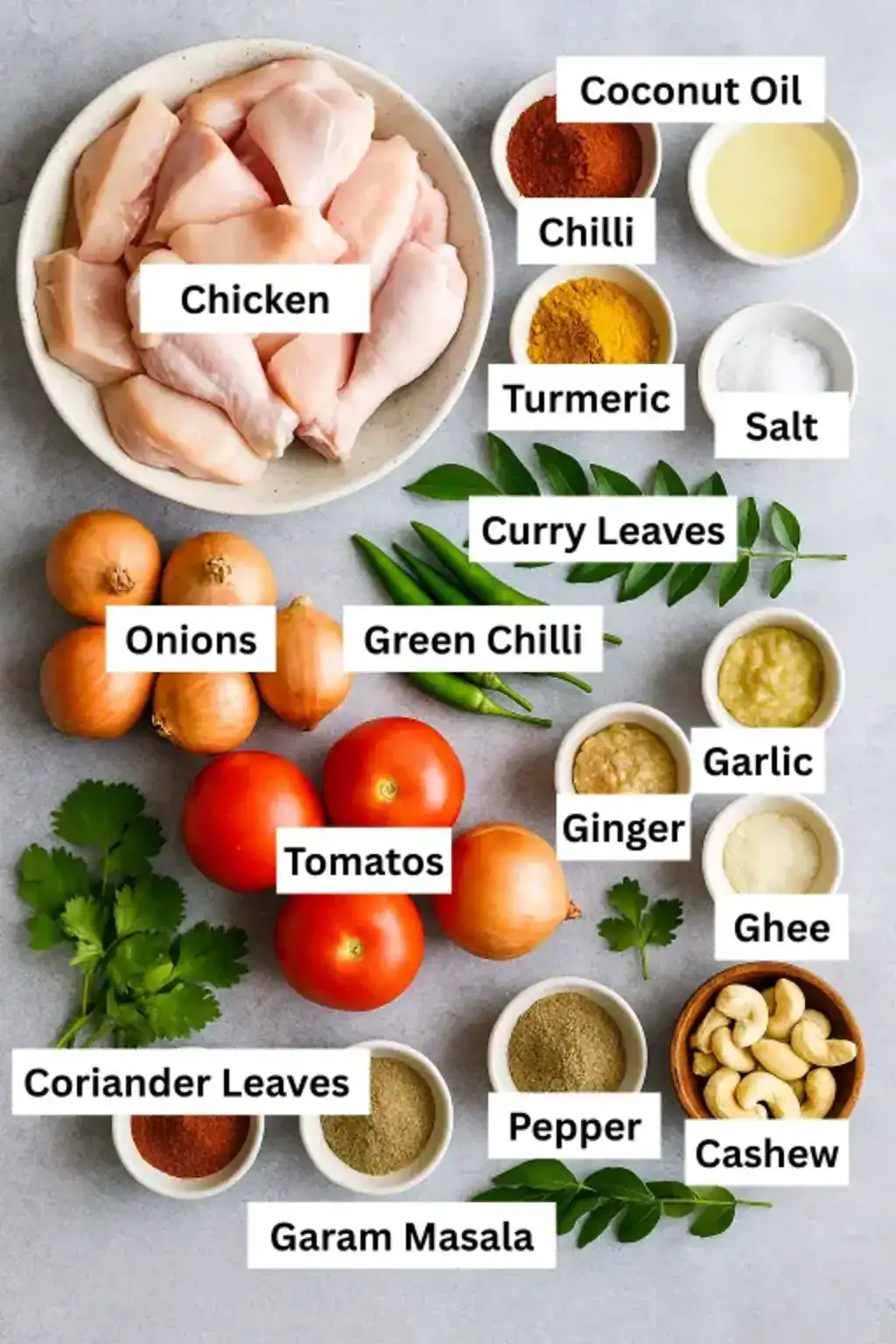 Chicken, spices, onions, tomatoes, herbs, oil, and ghee arranged on gray top for Kerala-style chicken roast preparation.