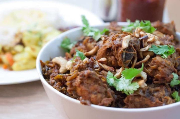 Kerala-style Nadan Kozhi Roast garnished with fresh coriander and fried cashews, served in a white bowl.
