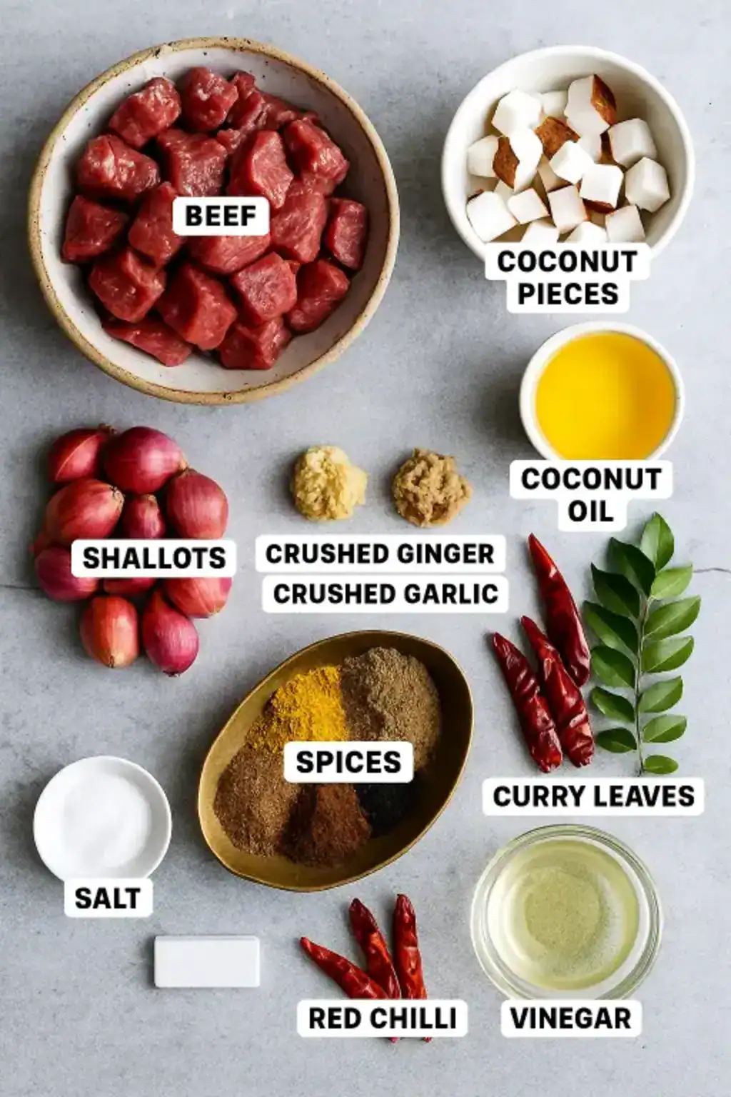 Beef cubes, coconut slices, shallots, spices, curry leaves, and oil arranged on a gray top for Kerala Style Beef Fry.