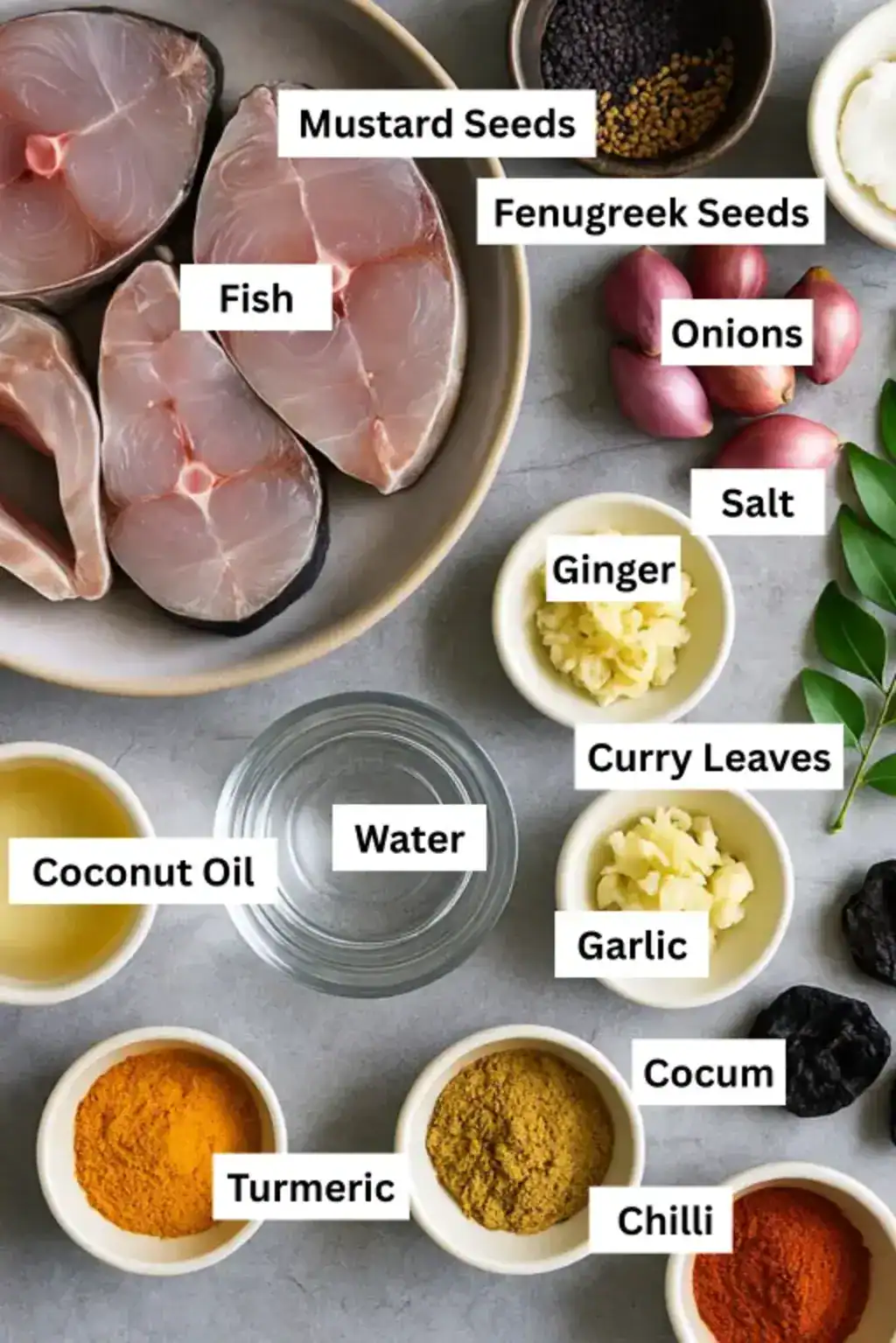 Fish curry ingredients on a gray surface, including fish slices, shallots, spices, curry leaves, cocum, oil, garlic, and ginger.