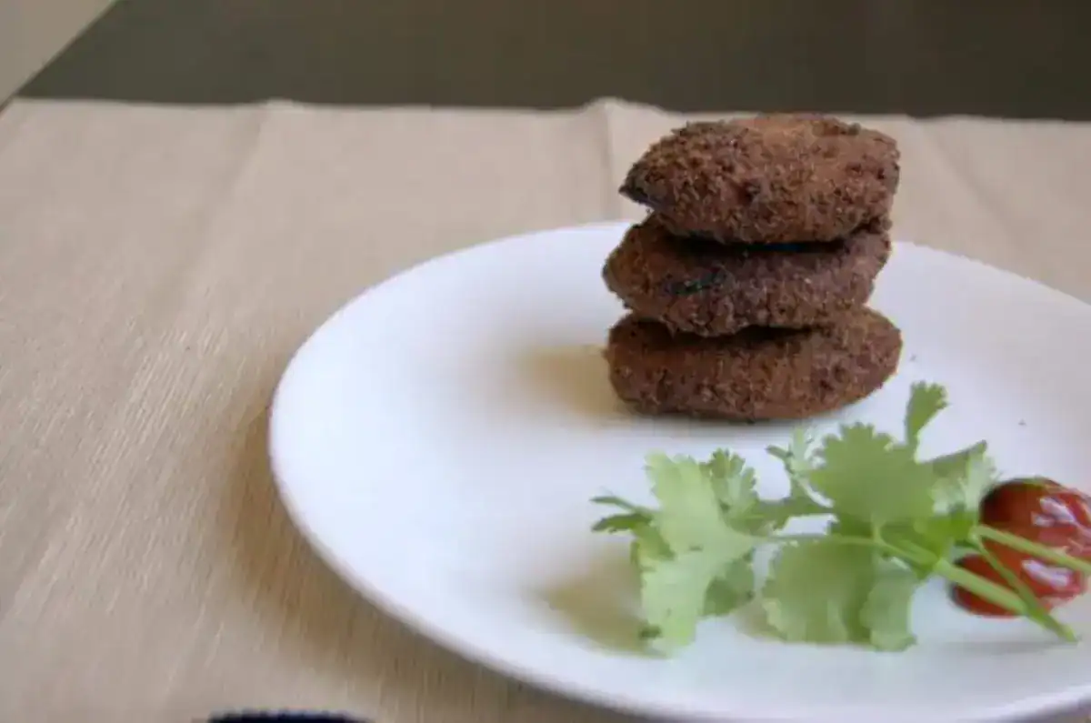 Kerala-style chicken cutlets stacked on a white plate, served with tomato sauce and fresh coriander garnish.
