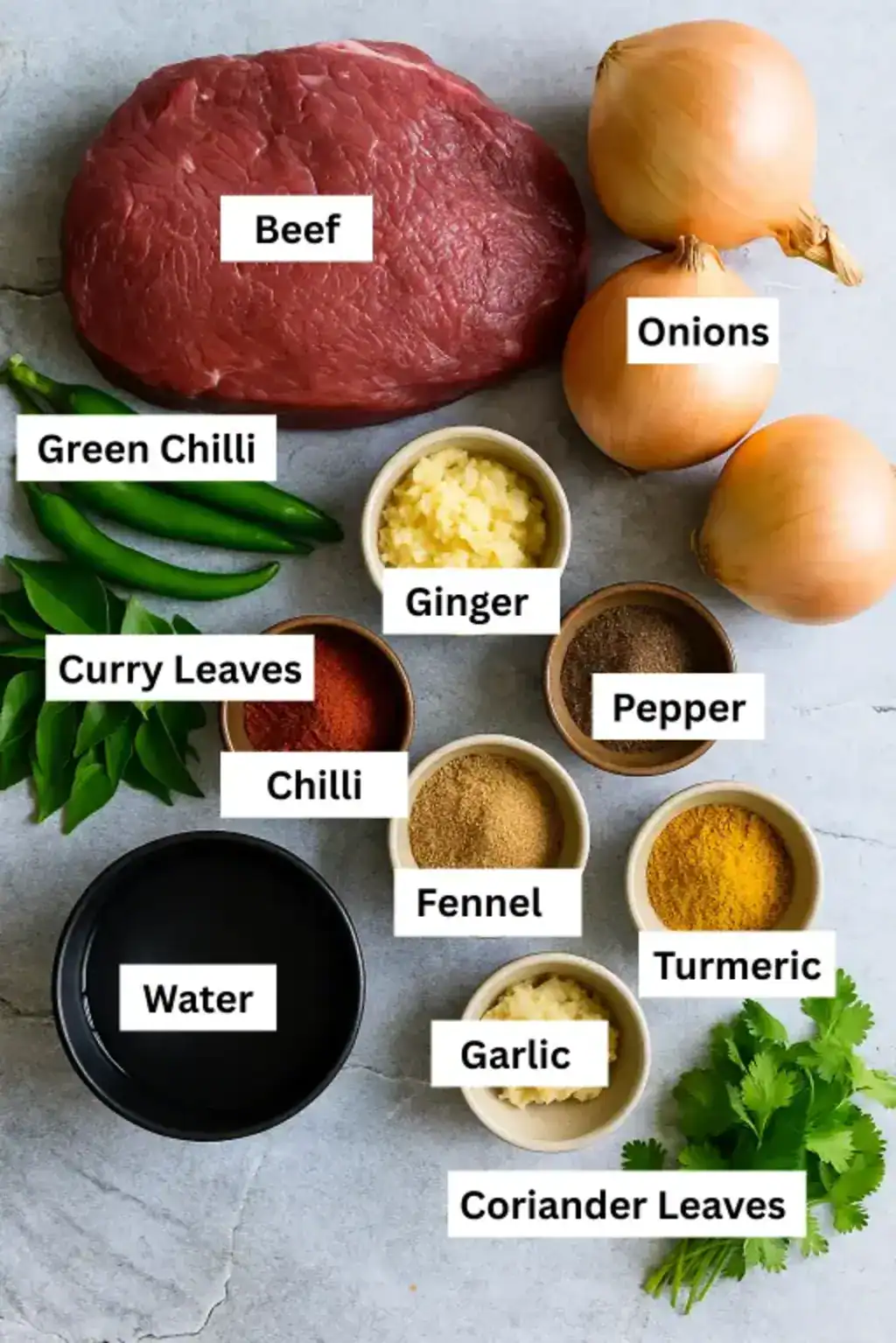 Beef Curry ingredients arranged on a gray surface, including beef, onions, chilies, spices, garlic, ginger, curry, and coriander leaves.