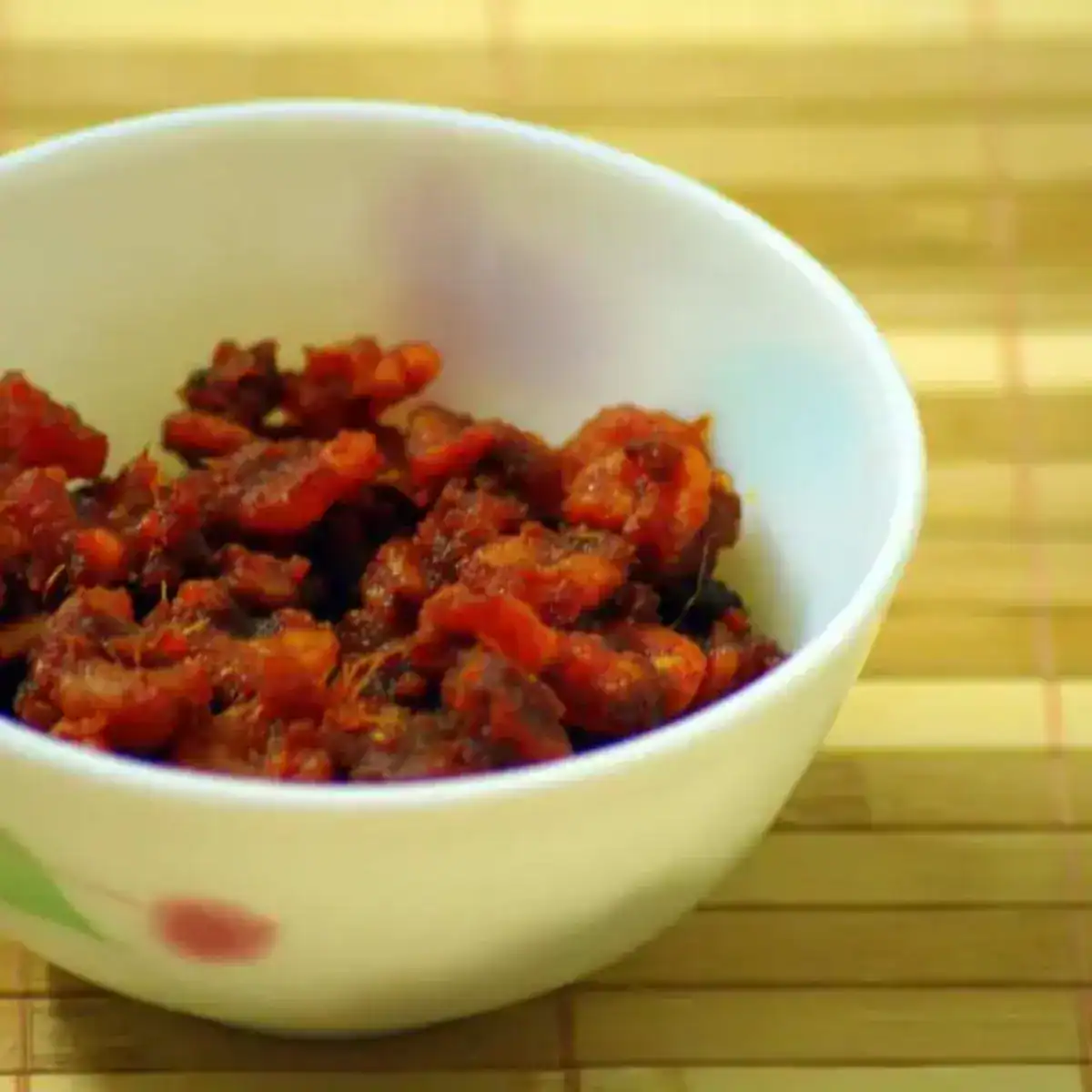 Kerala style shrimp pickle served in a white bowl on a bamboo mat surface.