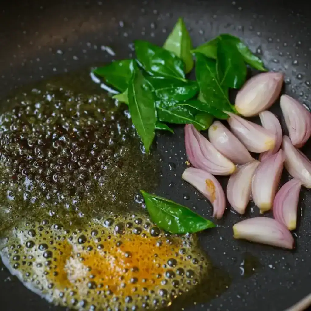 Curry leaves, shallots, and mustard tempering in coconut oil for Kappa Biriyani final garnish.