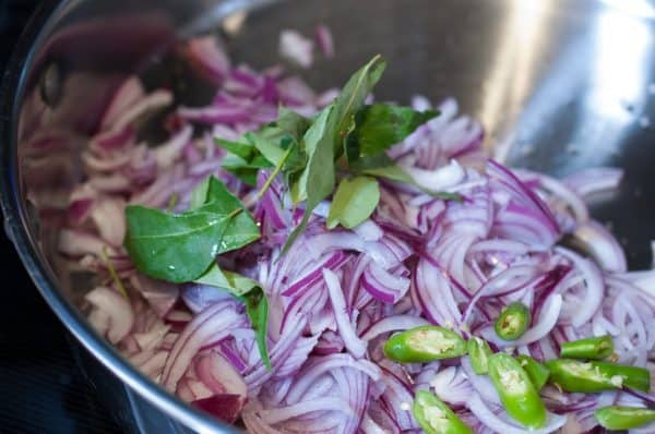 Sliced shallots, curry leaves, and green chilies are sautéing in oil.