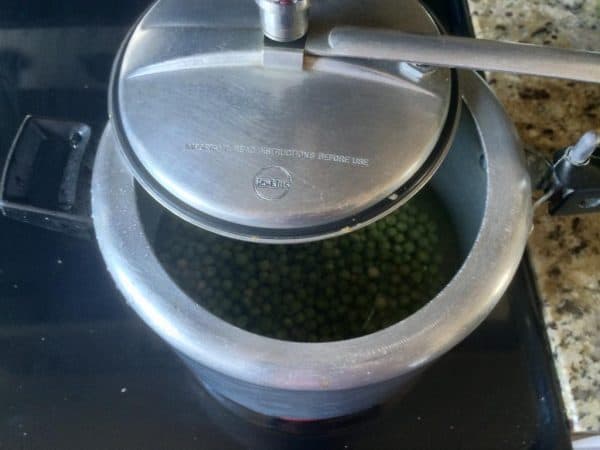 Green peas being pressure cooked in a steel cooker on the stove.