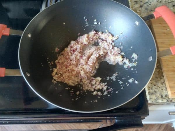 Finely chopped onion sautéing in coconut oil inside a black kadai.