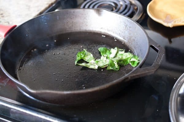 Curry leaves sizzling in hot coconut oil inside a cast iron pan for Achinga Payar Mezhukkupuratti.