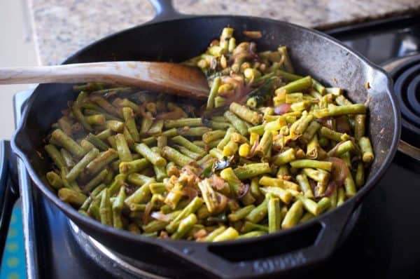 Long beans halfway cooked with onion, garlic, and spices in pan for Kerala-style stir fry.