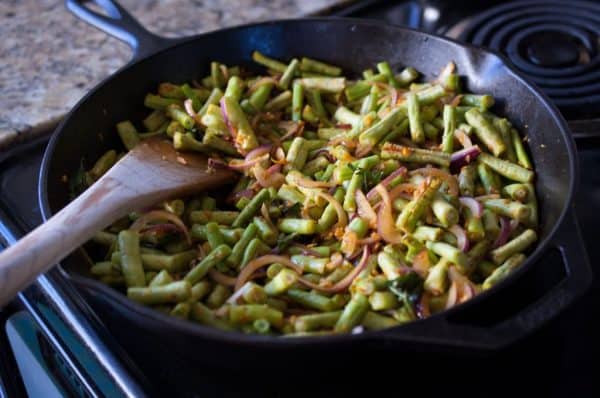 Chopped long beans, onion, and spices added to pan for making Achinga Payar Mezhukkupuratti.