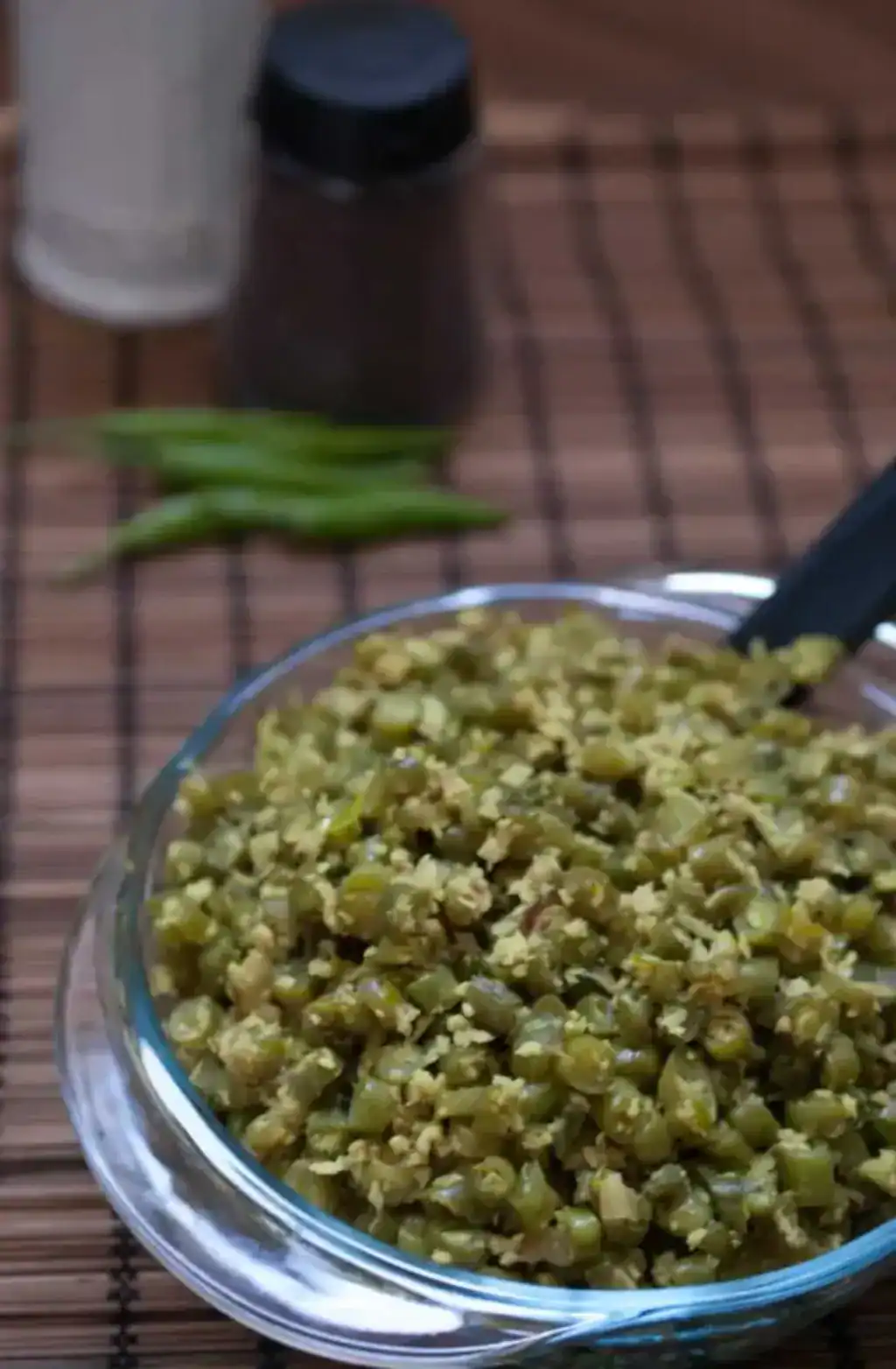 Close-up of Kerala-style beans thoran with coconut served in a glass bowl on a bamboo mat background.