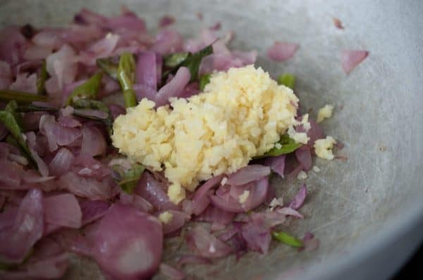 Ginger garlic paste added to sautéed onions, curry leaves, and green chilies in a pan.