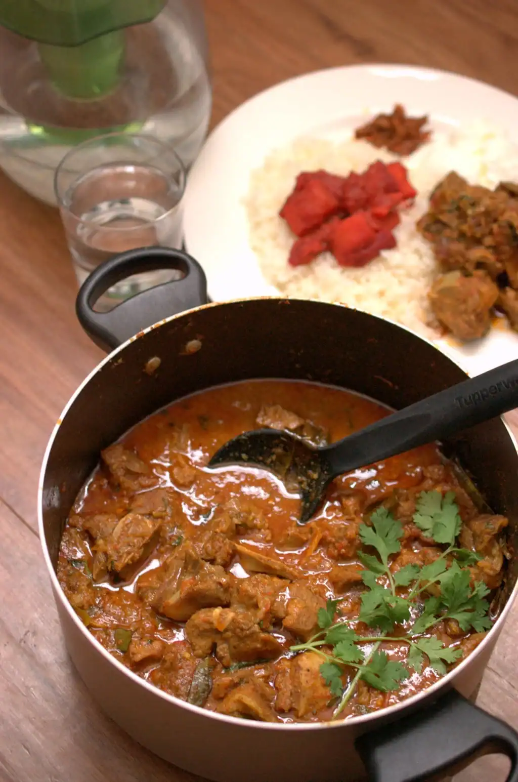 Kerala style mutton curry served hot in a nonstick pot with rice and pickle on the side, traditional lunch setting.