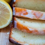 Glazed lemon yogurt cake slices on a wooden cutting board with a fresh lemon beside.