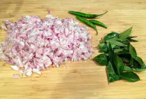Chopped small onion, green chilies, and curry leaves on a wooden board for Kerala mutton curry.
