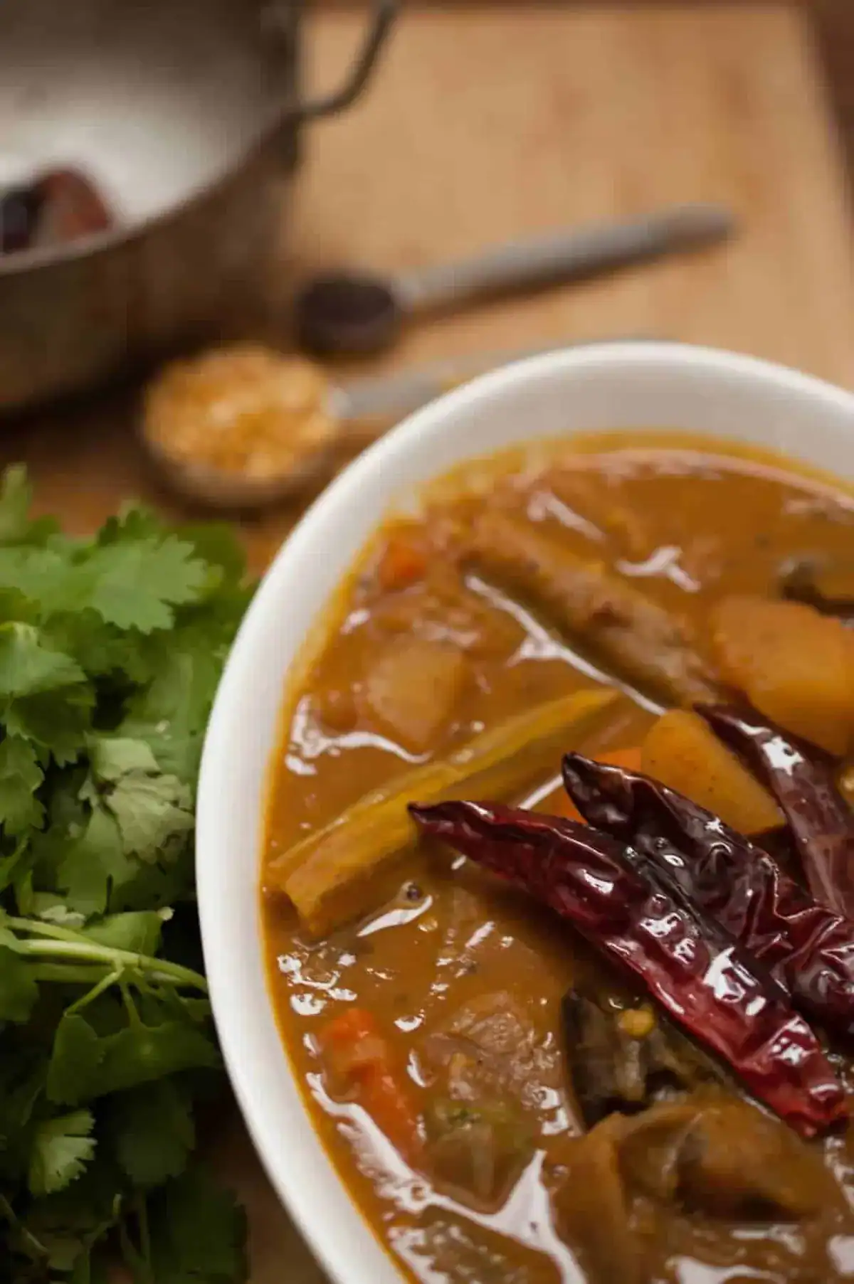 Kerala style sambar served in a white bowl with drumstick, potato, and dried red chillies, garnished with curry leaves.