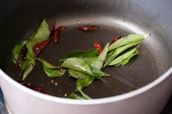Mustard seeds, curry leaves, and dried red chillies sizzling in hot oil inside a pan for Kerala sambar tempering.