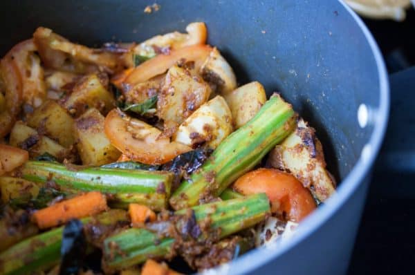 Drumstick, potato, carrot, and tomato sautéed with curry leaves and spices in a pan for Kerala sambar preparation.