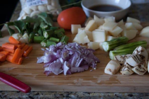 Chopped drumstick, brinjal, carrot, potato, okra, tomato, onion, and a bowl of tamarind water arranged on a board for Kerala sambar.