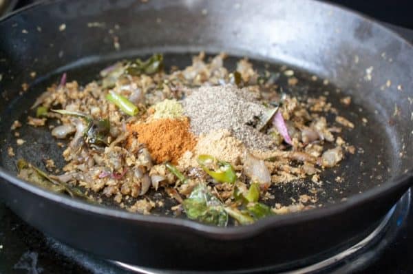 Adding turmeric, paprika, and black pepper to the pan for Nadan Pepper Fry.