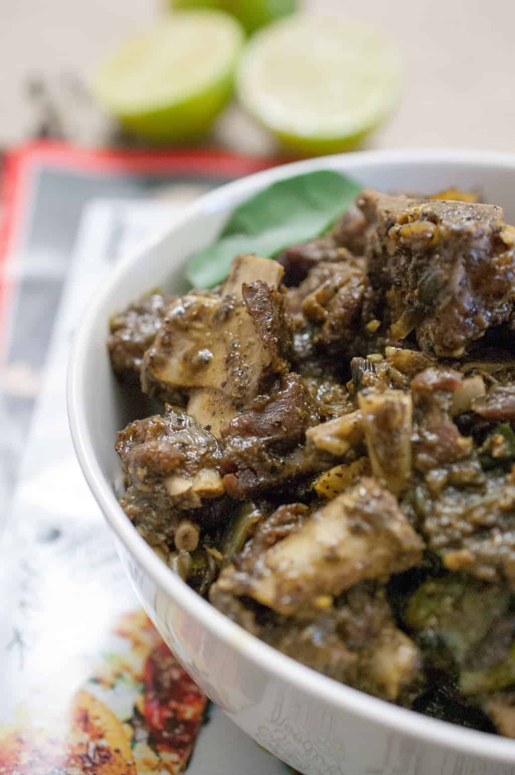 Kerala Style Mutton Fry, served in a white bowl with fresh lime wedges and curry leaves.