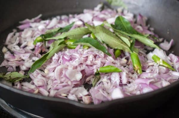 Sautéed onions, green chilies, and curry leaves in a cast-iron pan.