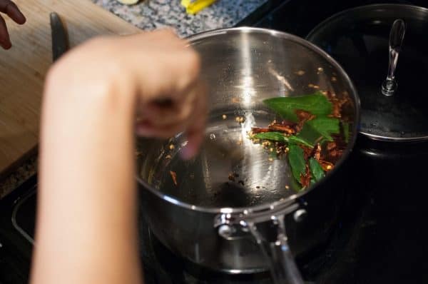 Mustard seeds, dried red chilli, and curry leaves spluttering in hot coconut oil in a pan for Moru Curry.