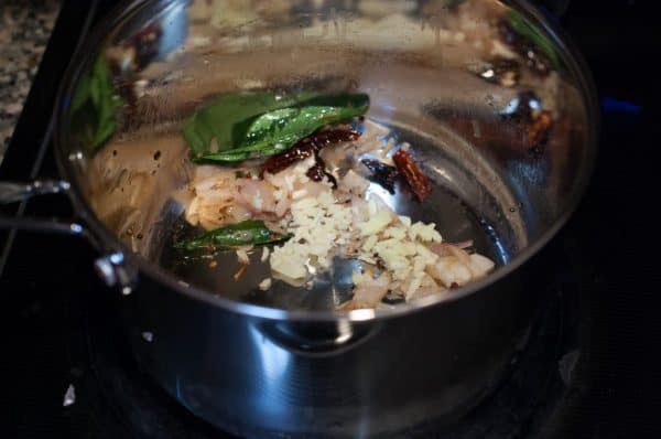 Chopped shallots, ginger, and garlic added to the tempering with curry leaves and dried chillies in a pan.