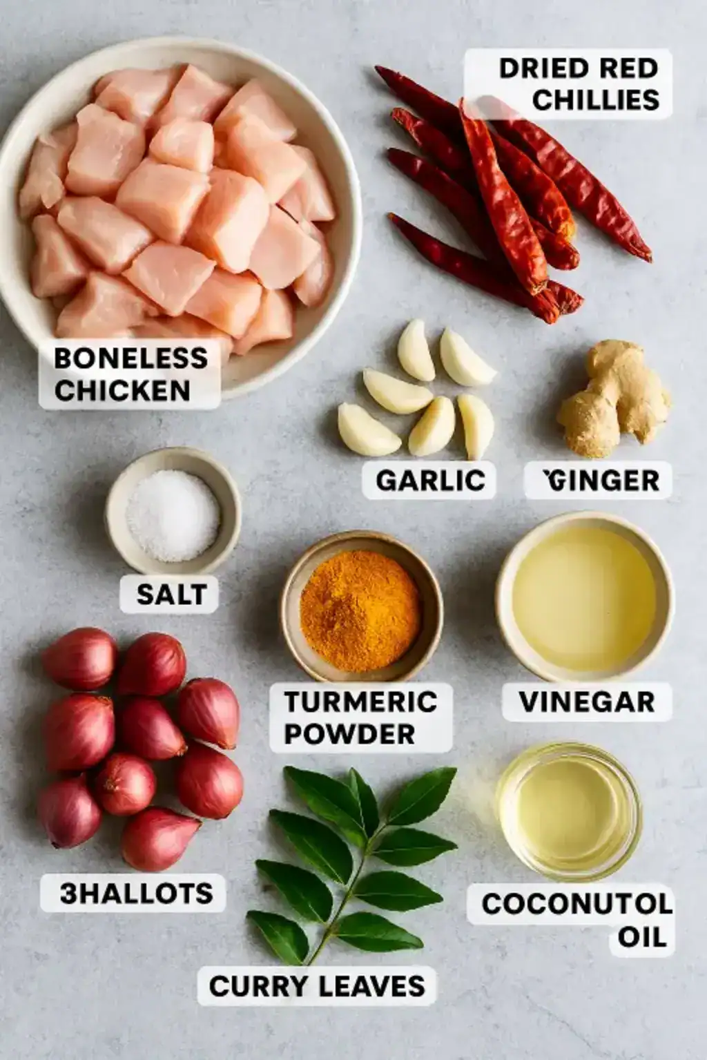 Ingredients for Kerala style chicken fry, including boneless chicken, spices, shallots, curry leaves, and oil on a on a gray surface.