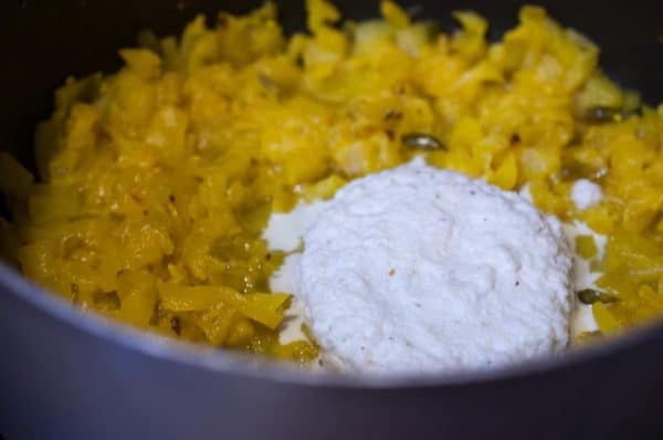 Ground coconut paste added to softened yellow pineapple mixture in a pan.