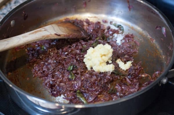 Ginger and garlic paste are added to sautéed onions while cooking Kerala prawns masala in a pan.
