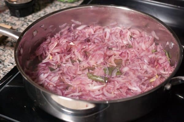 Sliced onions sautéing in coconut oil with curry leaves in a steel pan for chemmeen masala.