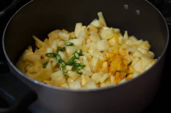 Pineapple chunks with turmeric and green chilli cooking in a black pan on stovetop.