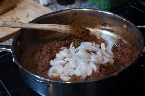 Raw prawns added to cooked masala base during nadan chemmeen masala preparation in a wide steel pan.