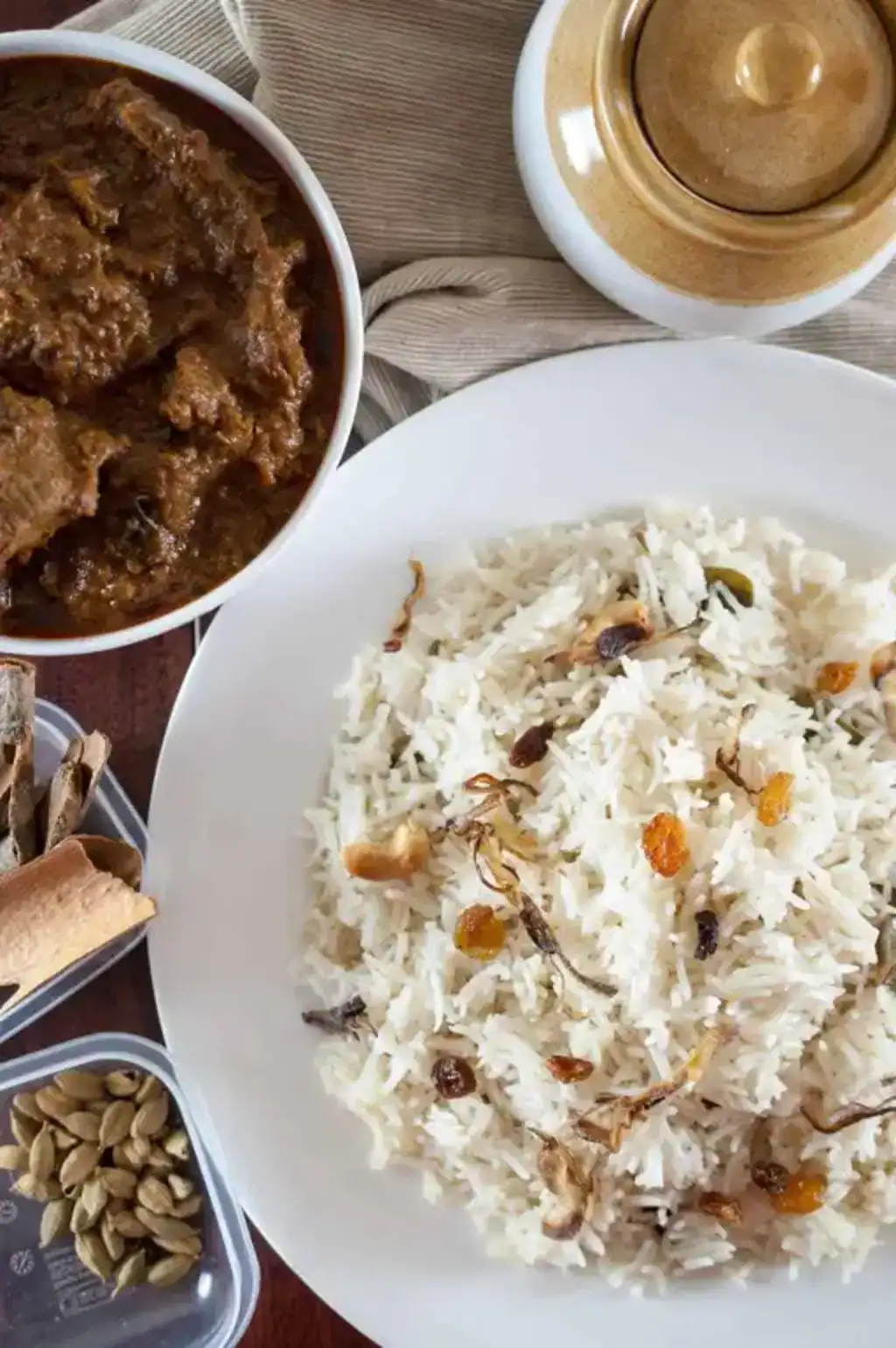Kerala Ghee Rice (Ney Choru) served with beef curry, topped with fried onions, raisins, and cashews on a white plate.