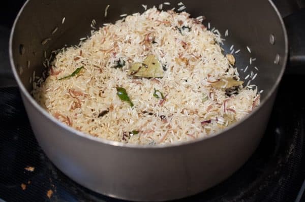 Uncooked rice is being sautéed with onions and whole spices before adding water.