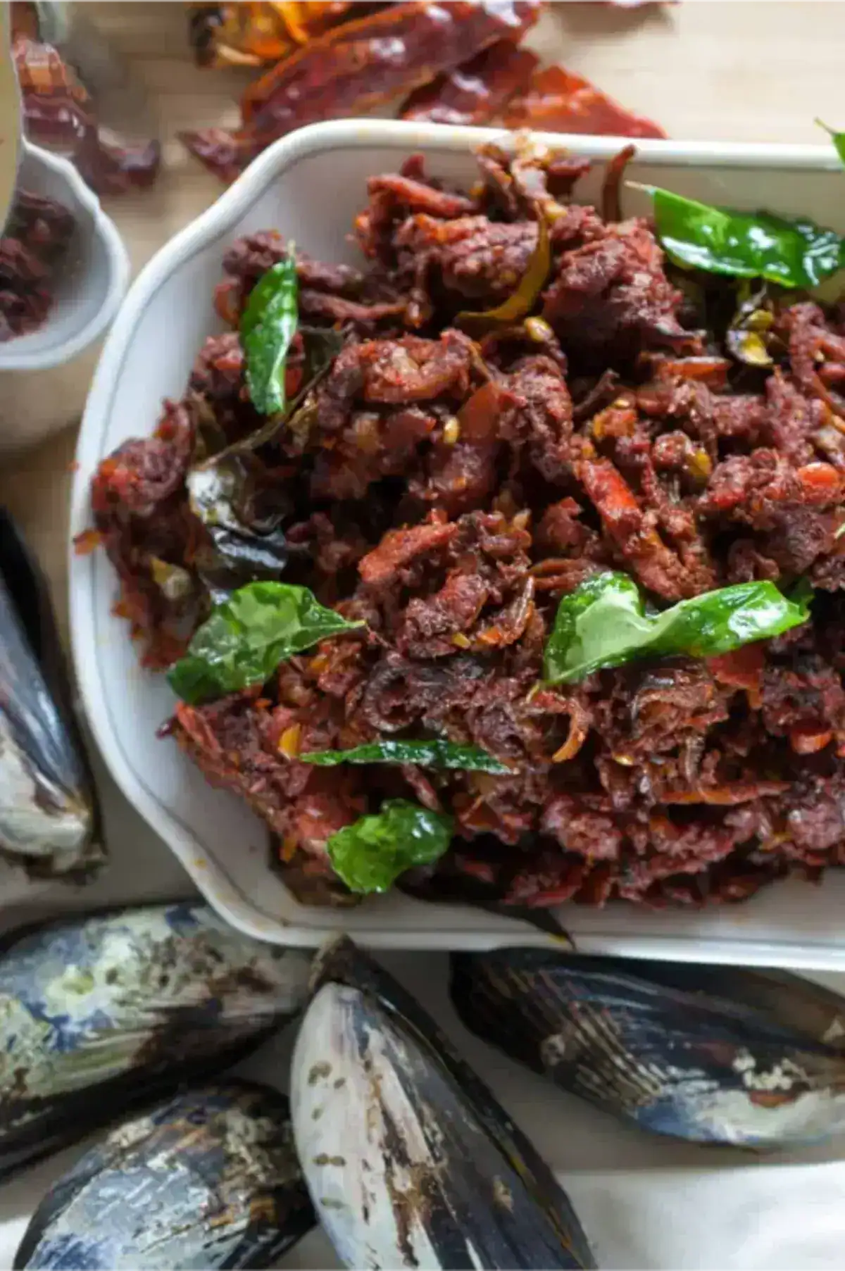 Kerala-style mussels fry (kallumakkaya varattiyathu) plated with curry leaves in a white plate.