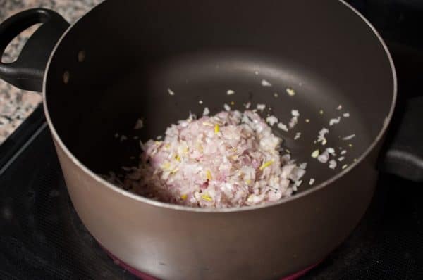 Chopped shallots added to a pan to begin the masala for kallumakkaya fry.