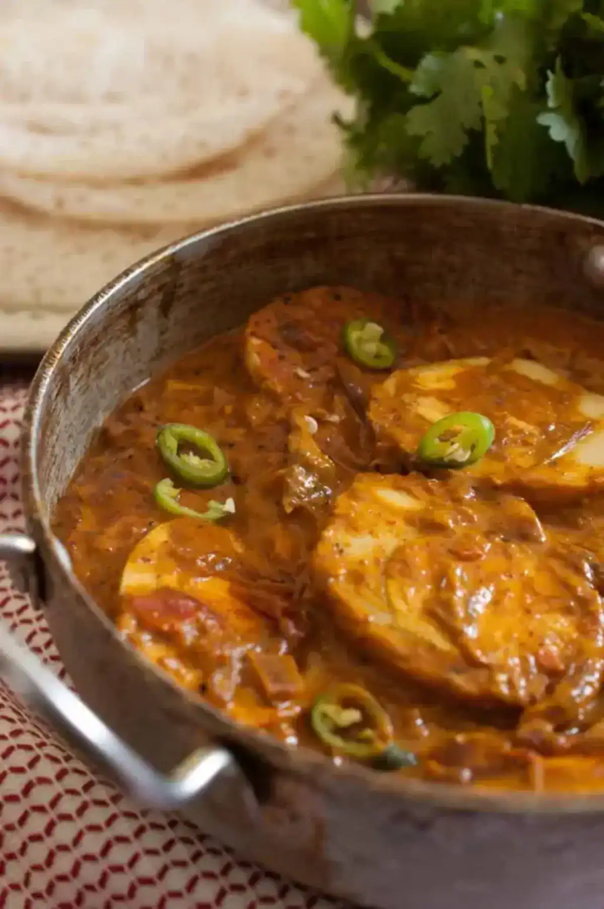 Kerala style egg curry with coconut milk simmering in a pan with sliced green chillies on top.