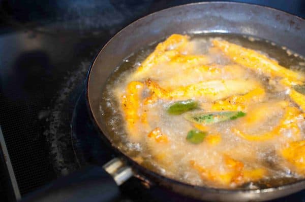 Netholi (anchovies) are being fried in hot coconut oil in a flat pan for Kerala Style anchovy fry.