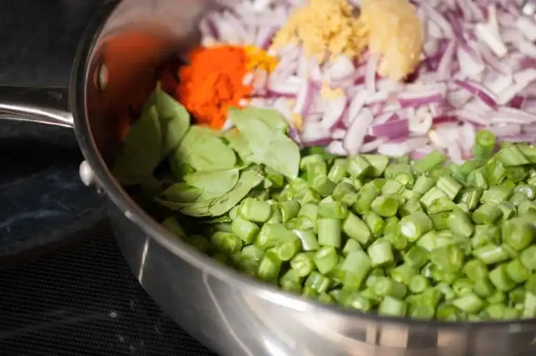 Chopped French beans, onion, curry leaves, and spices ready to cook for Payar Mezhukkupuratti.