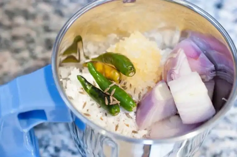 Coconut, green chilli, jeera, garlic, and shallots placed in a grinder jar for making the coconut mix.