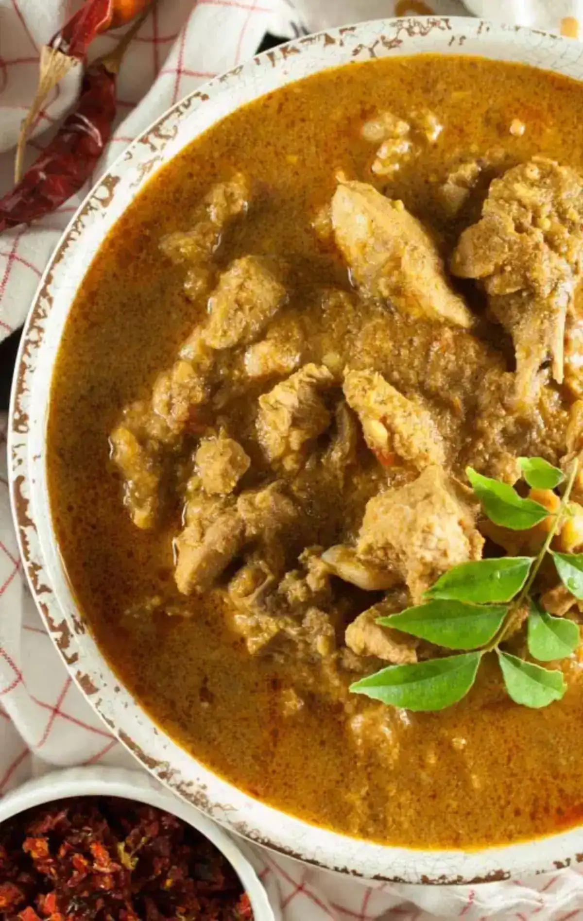 Varutharacha Chicken Curry (Kerala Chicken Curry with Roasted Coconut) served in a white bowl with curry leaves on top.