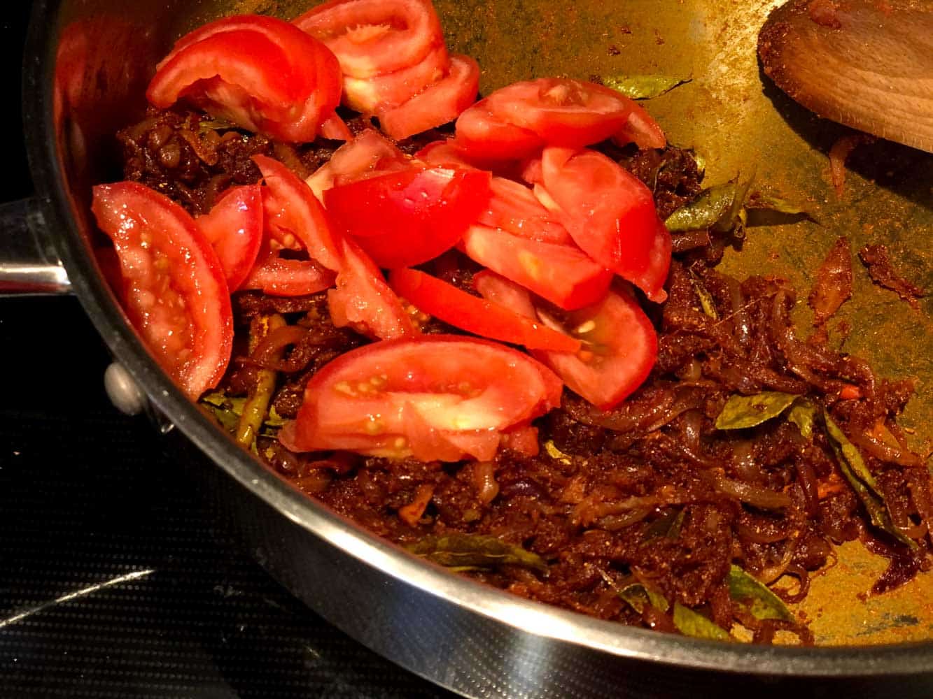 Adding sliced tomato into sauteed onion and masala mix